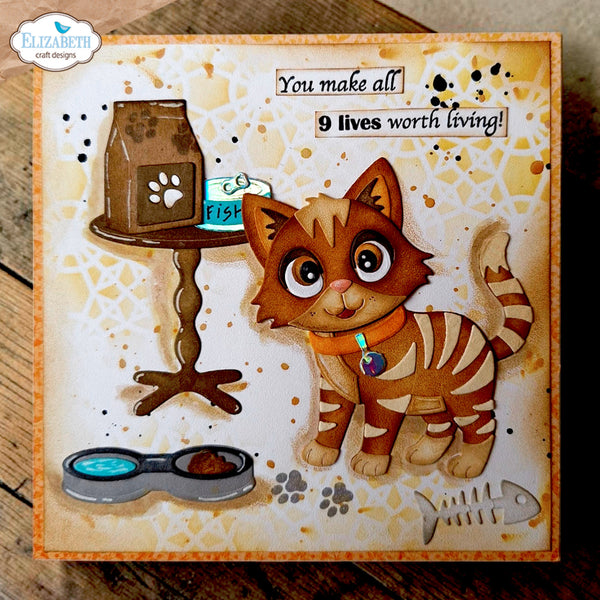 A square handmade greeting card featuring a cute cartoon orange tabby cat with paw prints, a small table with a cat bag, a fish, and the text 'You make all 9 lives worth living!'. The card is photographed on a rustic wooden surface, with a 'Elizabeth craft designs' logo in the top-left corner.