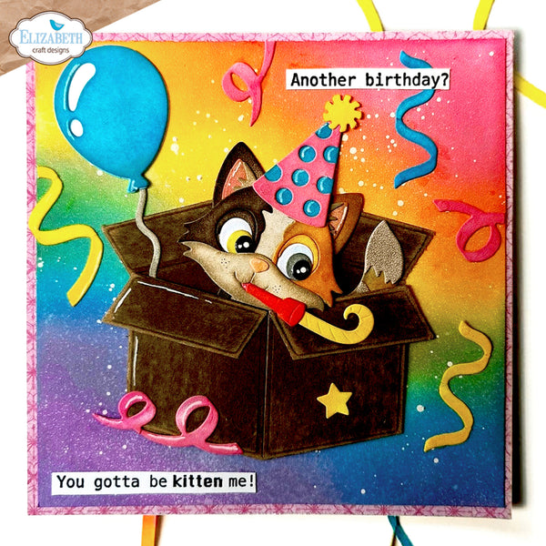 A handmade birthday card featuring a cartoon kitten peeking out of a box with a party hat and a party horn. The card has a colorful rainbow gradient background with confetti and streamers, and text reading 'Another birthday?' and 'You gotta be kitten me!'.