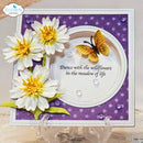 A handmade greeting card displayed on a clear stand, featuring three white paper daisies with yellow centers, a yellow and black butterfly, and purple patterned and white circular layers with the printed phrase 'Dance with the wildflowers in the meadow of life'.