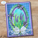 A handmade greeting card featuring a lavender and butterfly design, displayed flat on a rustic wooden surface. The card has a purple border, a blue and green textured background, purple lavender stems, three purple butterflies, and a white sheer bow at the bottom.