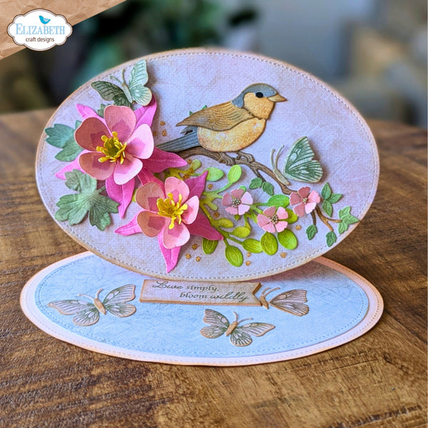 Two handmade oval paper cards displayed on a wooden surface. The top card is light lavender with a detailed illustration of a small bird perched among pink flowers, green leaves, and butterflies.