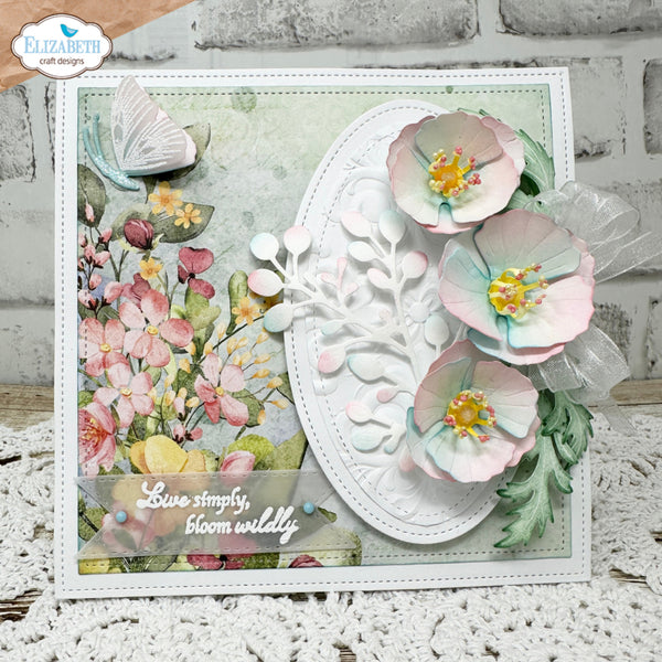 A handmade floral greeting card featuring three layered pastel pink and mint paper flowers, a white embossed oval center, and a watercolor-style floral panel on the left. The card is displayed on a white lace surface against a white brick wall background, with a 'Elizabeth craft designs' logo in the top-left corner.