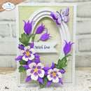 A handmade greeting card featuring a white and purple butterfly, purple and white pansies with green leaves, and a banner that reads 'With love'. The card is displayed on a white lace surface with a white brick wall background.