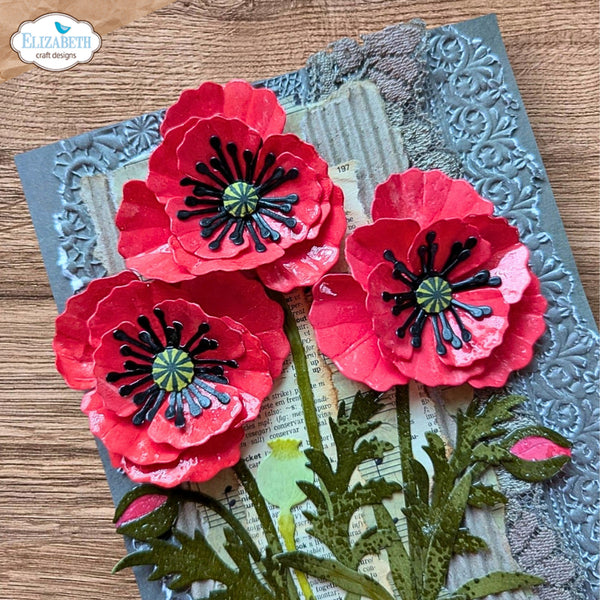 A handmade poppy card featuring three dimensional red paper poppies with black centers, layered over a gray embossed background and vintage book pages. A brand logo for 'Elizabeth craft designs' is visible in the top left corner.