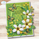 A handmade layered card featuring white flowers, yellow buds, green leaves, and butterflies on a textured green background, with the text 'Let us live like flowers, wild and beautiful and a-drenched in the.