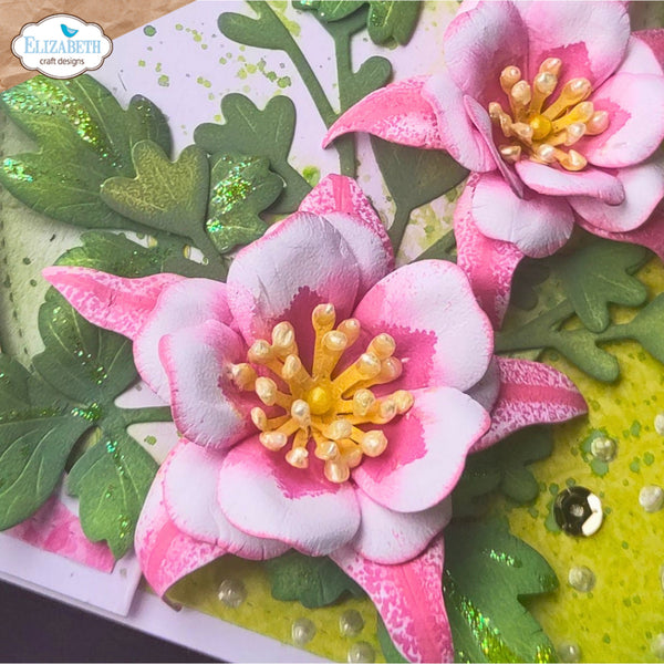 A close-up of a handmade floral card or craft embellishment featuring layered pink and white flowers with yellow centers, green textured leaves, and decorative pearl accents on a light background. A 'Elizabeth craft designs' logo is visible in the top-left corner.