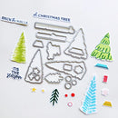 A flat lay of Christmas-themed crafting dies and decorative stickers on a white background. The set includes metal tree-shaped and ornament-shaped dies, plus sample stickers in green, blue, yellow, pink, and white with phrases like 'Deck the Halls,' 'of Christmas Tree,' and 'Tis the season.