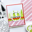 A handmade Christmas greeting card with layered red and white striped borders, green pine trees, and a central circular die-cut element reading 'Oh Christmas Tree,' shown on a white surface with crafting tools and patterned paper around it.