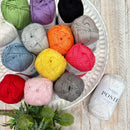 Assorted colorful Fiddle sticks Posie Yarn balls on a decorative plate with a plant in the foreground.