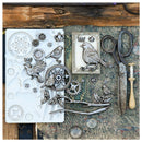 A flat-lay of metal craft embellishments featuring bird and gear designs, displayed alongside a white silicone mold, vintage-style scissors, a wooden spool, and a rustic wooden background.