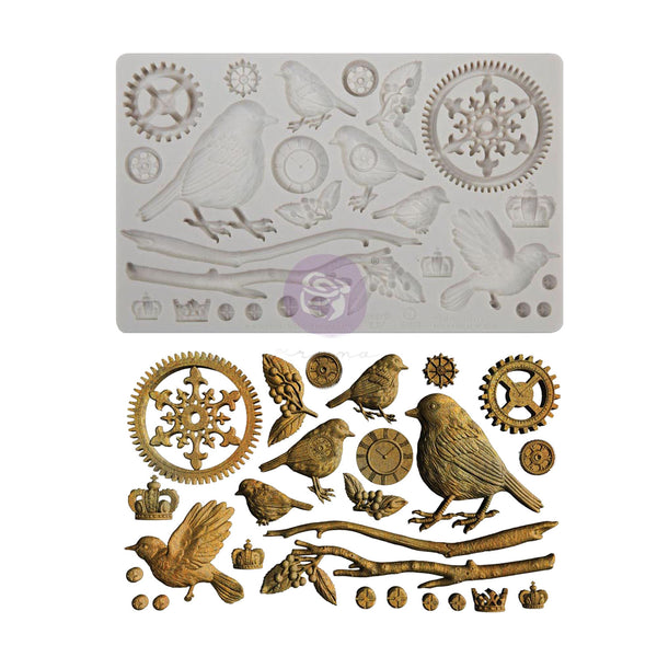 A silicone mold tray shown above its corresponding metal casting pieces, featuring bird, snowflake, gear, and branch motifs in a vintage engraving style.