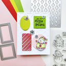 A handmade Christmas greeting card displayed on a styled flat-lay background with crafting tools, including metal die-cut frames, a laser-cut pattern sheet, and snowman-themed clear stamps.