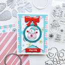 A handmade Christmas greeting card featuring a snowman illustration, a red bow, and a red banner that says 'stay cozy', surrounded by crafting tools, paper, and stamped designs on a white background.