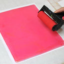 Person using a red roller on a pink sheet of paper with a grid background