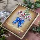 A handmade Christmas greeting card with a brown gradient background, featuring a blue bow, candy canes, holly leaves, and gold 'HAPPY HOLIDAY' text. The card is styled on a brown textured surface with green leaves and a glass ornament.