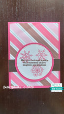 A handmade holiday greeting card with pink and white diagonal stripes, a brown horizontal band, and a circular white center featuring pink snowflakes and the message, 'May your holidays sparkle with moments of love, laughter, and goodwill.' The card is photographed on a dark brown wooden surface, with 'Beth Silaika © 2026' and 'gina k.