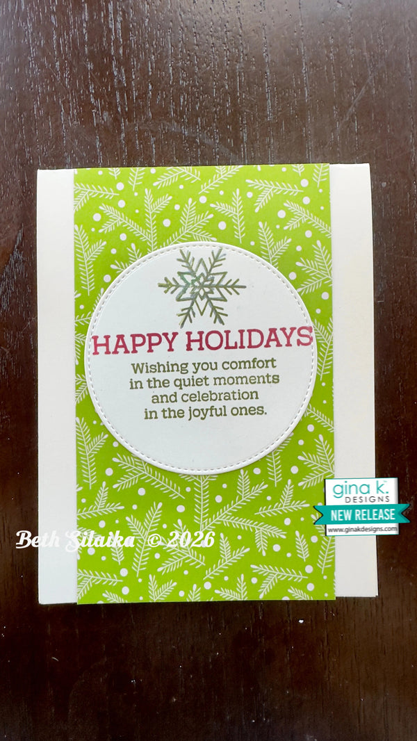A handmade holiday greeting card with a green and white patterned background, a white oval center, and the text 'HAPPY HOLIDAYS' in red. The card is photographed on a dark wooden surface, with Gina K.