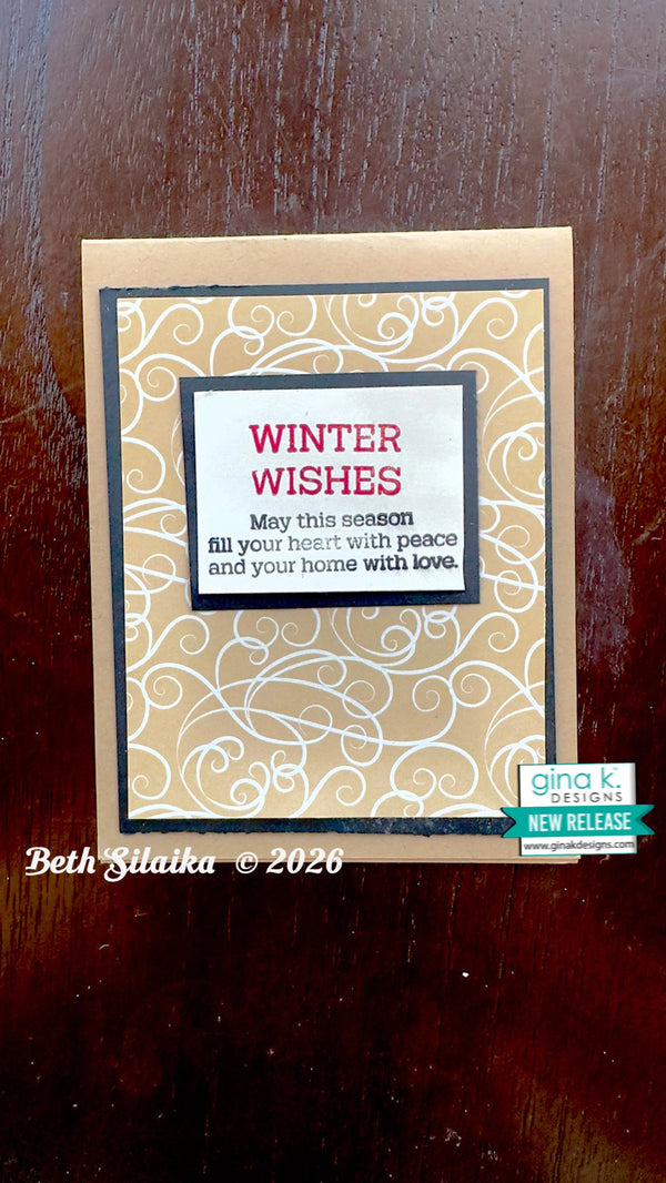 A handmade greeting card with a tan border, a beige and white scroll patterned background, and a central white label reading 'WINTER WISHES' in red, placed on a dark wooden surface. A 'gina k designs NEW RELEASE' sticker is visible on the lower right of the card.