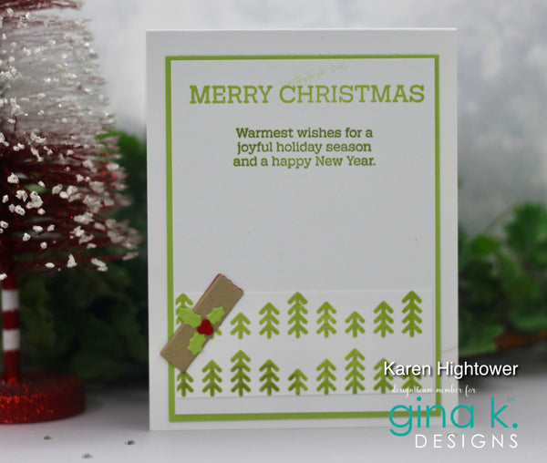 A handmade Christmas greeting card with green text reading 'MERRY CHRISTMAS' and a holiday message, decorated with green pine tree stamps and a small brown envelope with a red holly accent. The card is displayed on a white surface with blurred festive decorations in the background.