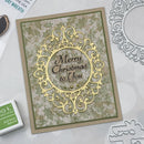 A handmade Christmas greeting card with an ornate gold laser-cut filigree frame and the words 'Merry Christmas to You' in the center, styled on a light gray surface with crafting tools and a Takor Designs ink pad nearby.