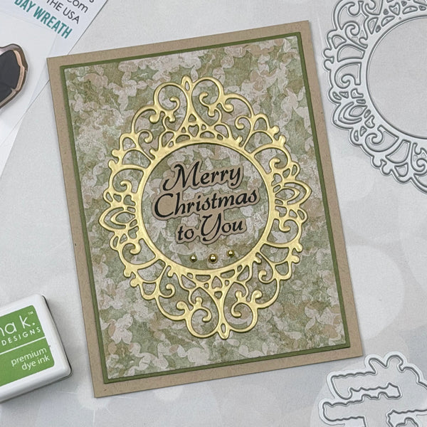 A handmade Christmas greeting card with an ornate gold laser-cut filigree frame and the words 'Merry Christmas to You' in the center, styled on a light gray surface with crafting tools and a Takor Designs ink pad nearby.