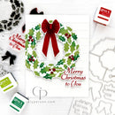 A handmade Christmas greeting card featuring a green holly wreath with a red bow and red berries, alongside the text 'Merry Christmas to You'. The card is styled on a white wood background with Gina K.