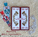 A handmade Christmas card with a red border and gold leaf scrollwork on a white background, featuring the text 'crack open THE HOLIDAY magic'. Two nutcracker paper cutouts are placed to the left on a beige textured crochet blanket, with a white die-cut floral overlay on the right.