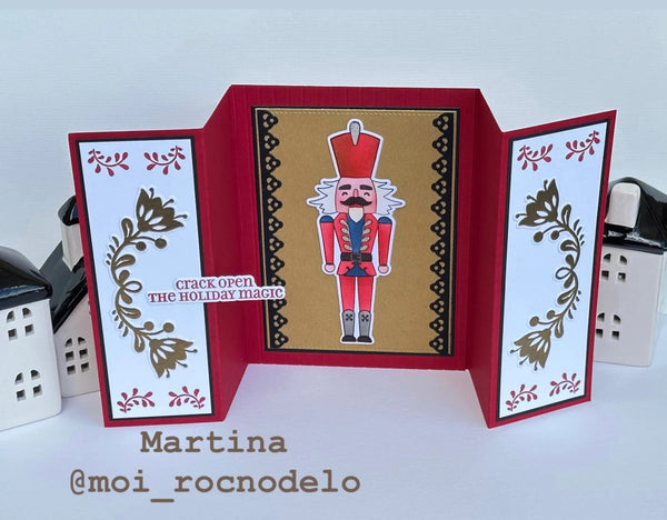 A handmade holiday pop-up card featuring a nutcracker illustration in the center, flanked by white panels with gold floral designs and red borders. The left panel includes the text 'crack open the holiday magic' and the name Martina with handle @moi_rocnodeleo is printed below the card.