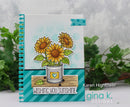 A handmade spiral-bound greeting card featuring three yellow sunflowers in a white bucket with green leaves, set against a light blue polka-dot background and teal striped accents. The card is displayed upright with green foliage in the background, and the text 'Karen Hightower' and 'gina k.
