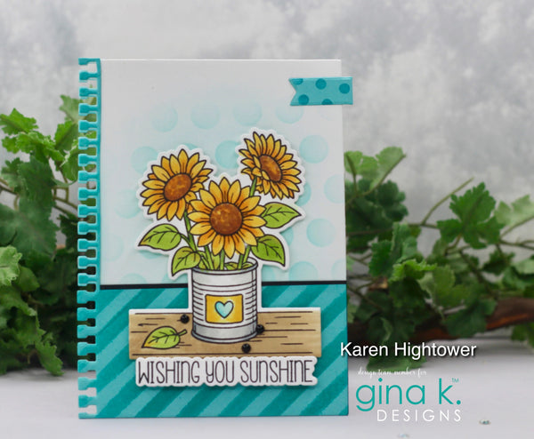A handmade spiral-bound greeting card featuring three yellow sunflowers in a white bucket with green leaves, set against a light blue polka-dot background and teal striped accents. The card is displayed upright with green foliage in the background, and the text 'Karen Hightower' and 'gina k.