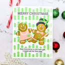 A handmade Christmas greeting card featuring two gingerbread cookies, one in a pink dress and one in a top hat with a green bow, on a white background with green pine tree patterns. The card is styled on a marble surface with holiday ornaments and candy canes.