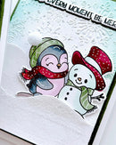 A close-up of a handmade holiday greeting card featuring a penguin and a snowman in winter clothing, with embossed snowflake details and the text 'EVERY MOMENT BE MERRY' at the top.