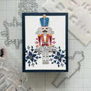 A handmade Christmas nutcracker card featuring a colorful stamped nutcracker figure with the text 'A LITTLE NUTTY ABOUT CHRISTMAS' and blue floral motifs, displayed on a gridded cutting mat with metal and plastic craft dies around it.
