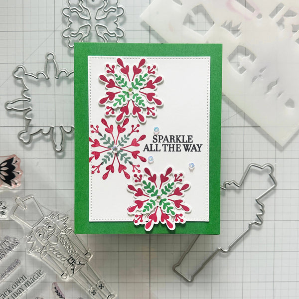 A handmade holiday card featuring three layered die-cut snowflakes in red and green on a white background with a green border. The card has the text 'SPARKLE ALL THE WAY' in black.