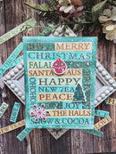 A handmade Christmas greeting card with a turquoise background and layered wooden-textured strips featuring holiday phrases like 'Have a Merry Christmas' and 'HAPPY NEW YEAR'. The card is styled on a rustic wooden surface with scattered matching paper strips, white beads, and dried flowers.