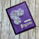 A handmade purple greeting card with a laser-cut damask pattern, featuring three layered white paper flowers with gold centers and the text 'YOU ARE Gorgeous' on a rustic wood background.