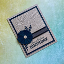 A handmade greeting card with a beige base, featuring a navy blue scalloped border, an embossed floral pattern, a matching navy blue paper flower with a crystal center, and the text 'Have a fabulous BIRTHDAY'. The card is photographed at an angle on a textured, iridescent yellow-to-blue background.