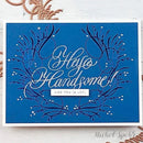 A square blue greeting card with white and dark blue decorative script and floral line art, plus the phrase 'Hello Handsome! LIKE YOU (A LOT)' in the center, photographed on a light surface with copper-colored decorative elements around it.