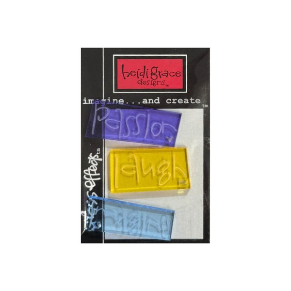 A package of three rectangular acrylic block in purple, yellow, and blue, featuring embossed words 'passion', 'laugh', and other words. The packaging has a black background with a red logo reading 'heidigrace designs'.