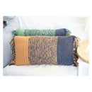 Two rectangular woven throw pillows with fringe, displayed on a white sofa. The front pillow is mustard yellow, heathered navy, and slate blue.