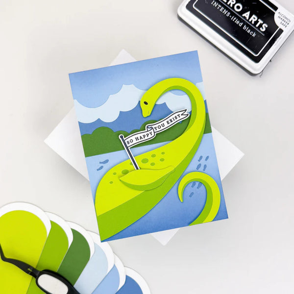 Card with a green dinosaur illustration on a blue background, surrounded by additional cards and a stamp.