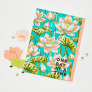 Notebook with floral design and 'One Day at a Time' text on a white background