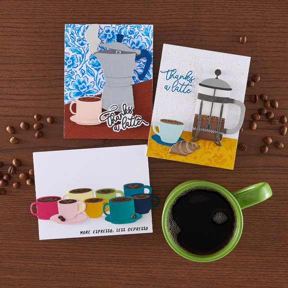 Three coffee-themed greeting cards on a wooden surface with coffee beans and a green mug.
