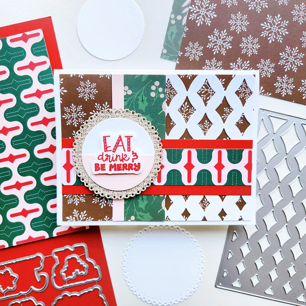 A handmade Christmas-themed greeting card with layered holiday patterns in green, red, brown, and white, featuring a central circular die-cut label that reads 'EAT drink? BE MERRY.' Surrounding the card are coordinating patterned paper sheets, a metal die, and white circular paper doilies on a light background.