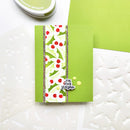 A handmade greeting card with a green background, a vertical white holly pattern strip with red berries, and a silver glitter border, alongside white embossed paper dies and a green ink pad.