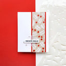 A handmade greeting card with a white left panel, a vertical beige patterned center panel with red berry motifs, and a small white banner reading “DECK THE HALLS,” shown on a red and white background with a white embossed holiday tree sheet behind it.