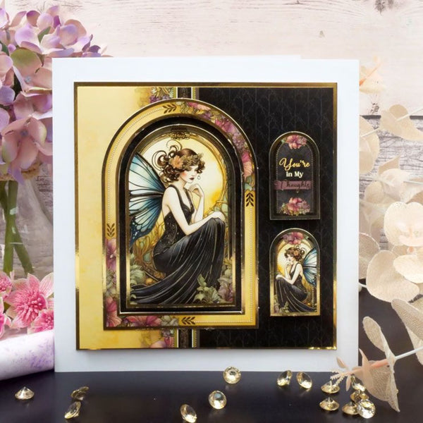 Decorative card with fairy design and floral elements on a wooden surface.