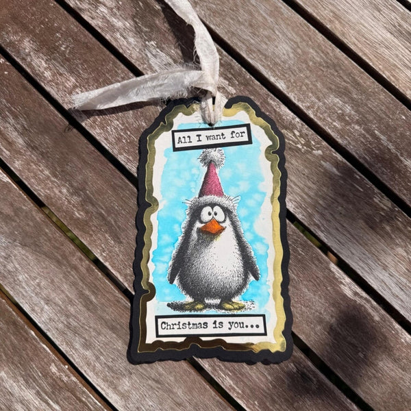 Gift tag with a penguin illustration and text on a wooden surface