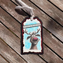 Decorative tag with a reindeer illustration and text 'Naughty is the new nice' on a wooden surface.