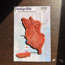 An IndigoBlu fairy-shaped rubber stamp in orange-brown ink, mounted on its light blue printed backing card, photographed on a dark wooden surface.